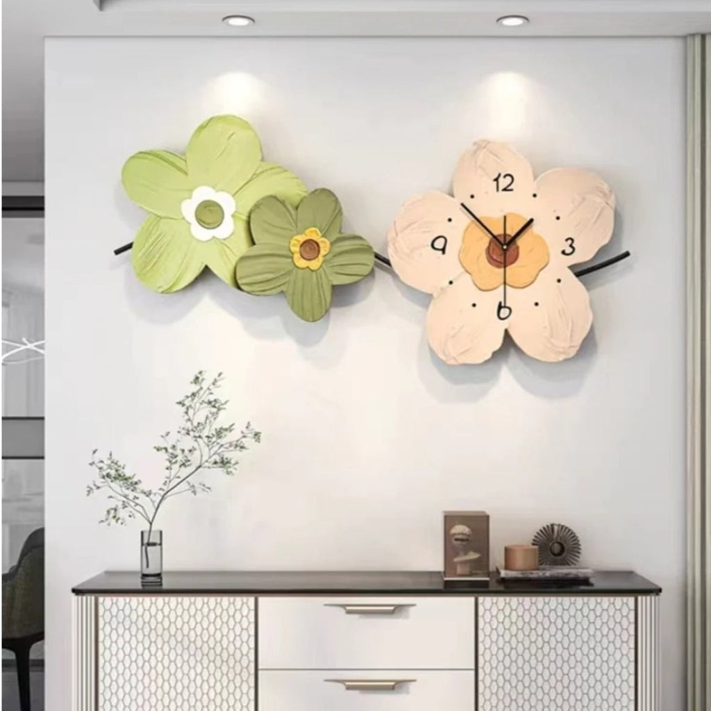 Three-flower wall clock with a beige, green, and brown color scheme, with the clock face integrated into the design of the flowers, mounted on a white wall above a light-colored cabinet.